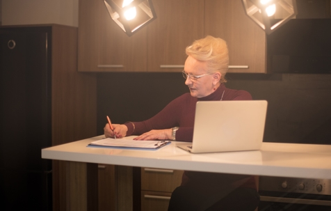 elderly woman doing some notes while in front of laptop
